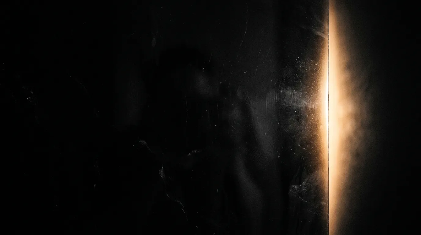 Warm light breaking through a narrow crack in darkness, the moment before everything opens up